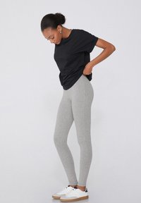 Leggings gris ajustés, associés à un t-shirt noir ample et des baskets blanches à semelle en caoutchouc. Tissu simple et extensible.