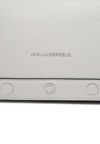 Borsa bianca in pelle con superficie testurizzata, caratterizzata da un logo argentato, bottoni a pressione e dettagli scuri. Design elegante dallo stile minimalista.