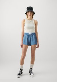Light blue cotton shorts with an elastic waistband and white drawstring, paired with a cream tank top and a black bucket hat. Black high-top sneakers.
