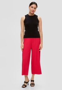 Zwarte geribbelde mouwloze top gecombineerd met felrode geplooide culottes en zwarte haksandalen. Soepele textuur met een vloeiende stofdetail.