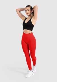 Brassiere sportivo nero a coste e leggings rossi a vita alta, abbinati a scarpe da ginnastica bianche. Texture liscia, design aderente e colori vivaci.