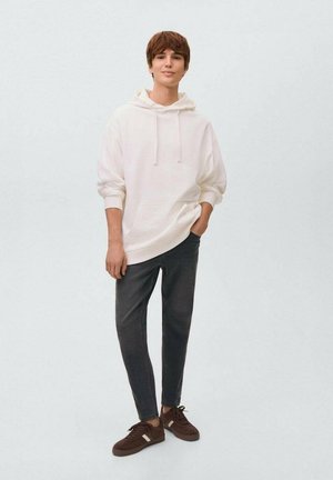 Weißer Hoodie mit Kängurutasche, kombiniert mit dunkelgrauen tapered Pants und braunen Wildledersneakern. Einfaches Design mit lässigem Schnitt.