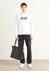 Fehér kapucnis pulóver fekete és piros "CALVIN KLEIN" logóval, fekete farmernadrág, fekete táska és fehér sportcipő. Sima anyag és letisztult dizájn.