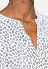 Blusa bianca con un motivo a foglie blu navy, scollo a V, maniche corte e vestibilità morbida, realizzata in tessuto leggero.