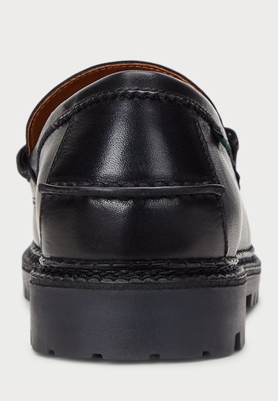 Zapato de cuero negro con un talón redondeado, costuras visibles y una suela de goma texturizada. Superficie lisa y detalles de diseño curvados.