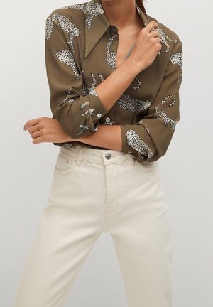 Olijfgroene blouse met witte panterprint, gestructureerde kraag en opgerolde lange mouwen, gecombineerd met crèmekleurige rechte jeans.