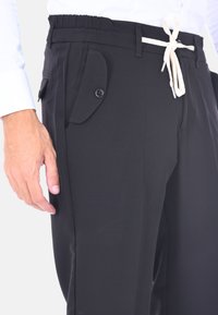 Pantaloni neri con elastico in vita, cordino regolabile, tasca laterale con pattina e dettaglio con bottone. Realizzati in tessuto morbido con una vestibilità tailored.