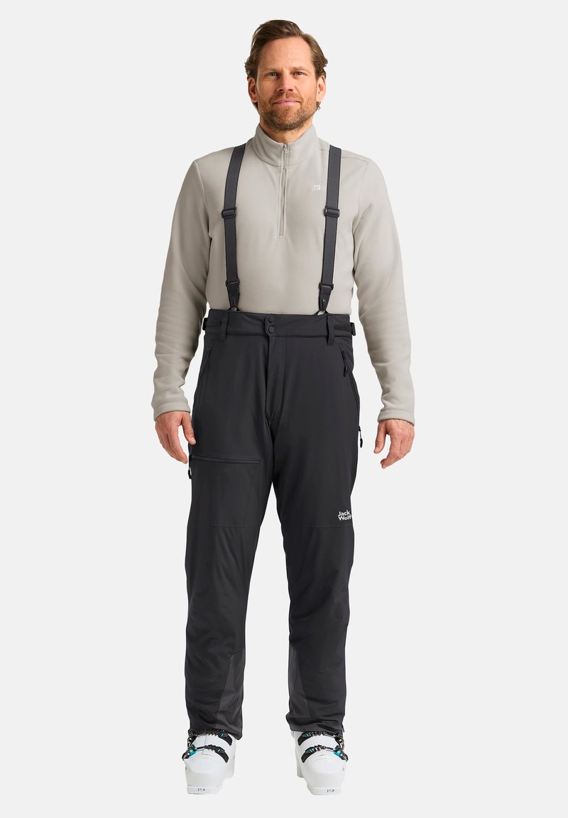 Pantaloni da neve neri con bretelle regolabili, tasche con zip e logo. Indossati sopra un pile grigio chiaro con colletto a mezza zip.