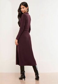Rochie burgundă cu mâneci lungi, cu talie accentuată printr-un cordon și fustă cu despicătură. Asortată cu cizme negre, cu toc înalt, până la genunchi. Textură de stofă netedă.