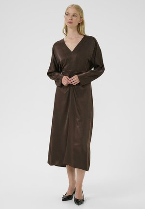 Satin brown dress with a V-neck, long sleeves, and a ruched waistline, falling to mid-calf, paired with black pointed shoes.