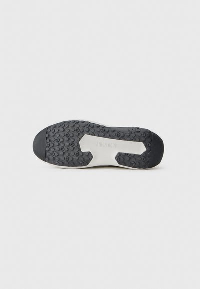 Suela de goma negra con una superficie texturizada, que presenta un acento blanco en la sección media y el logo en relieve "MOON BOOT".