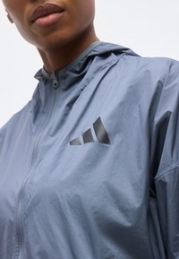 Gros plan d'une personne portant une veste zippée bleu clair avec un logo Adidas noir sur la poitrine.