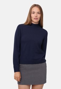 Maglione in maglia blu navy con collo alto e maniche lunghe, realizzato in un materiale morbido. Abbinato a una mini gonna a quadretti grigia.