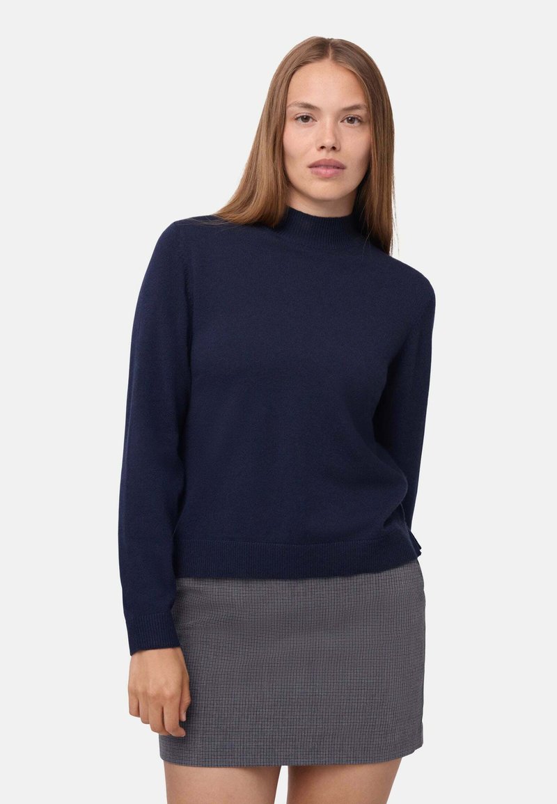 Maglione in maglia blu navy con collo alto e maniche lunghe, realizzato in un materiale morbido. Abbinato a una mini gonna a quadretti grigia.