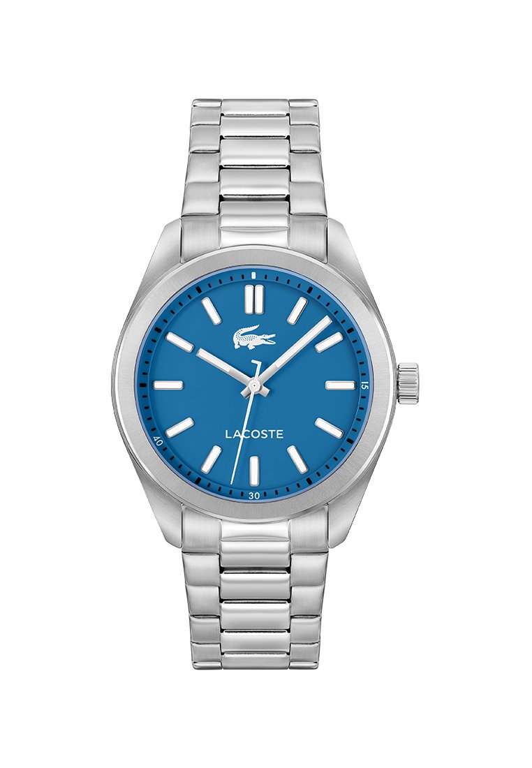 Reloj de pulsera de metal plateado con esfera azul, marcadores de hora blancos, logo de Lacoste y tres agujas que muestran las 10:12:37.