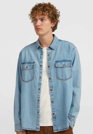 Light blue denim shirt with two chest pockets, button closure, and contrasting stitching. Features a relaxed fit and long sleeves.
