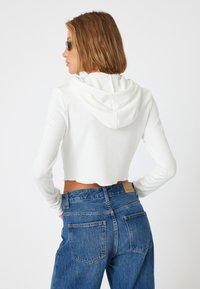 Witte cropped hoodie van ribbelstof met een capuchon, gecombineerd met hooggetailleerde blauwe spijkerbroek met achterzakken en een klassiek ontwerp.