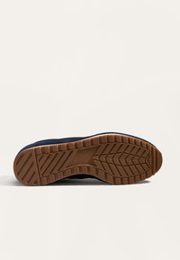 Tengerészkék sportcipő gumitalppal, textúrált tapadós mintával. A felsőrész puha anyagból készült, kontrasztos bézs díszítéssel.