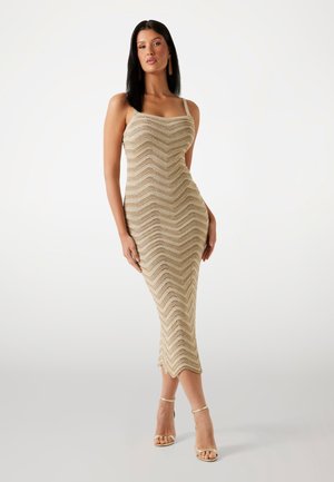 Dzianinowa sukienka w beżowym kolorze z wzorem zygzaków, dopasowany fason i długość do pół łydki. Posiada cienkie ramiączka i falbankowany dół.