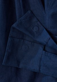 Tessuto di lino blu navy, texturizzato, con un polsino piegato e un dettaglio a bottone. Finitura liscia con leggere variazioni nella trama.