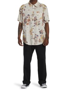 Lyhythihainen kukkakuvioinen paita, jossa vaalea kermanvärinen kangas, kirkkaanväriset kukat, napitettava etuosa ja rintatasku, yhdistetty mustiin housuihin.