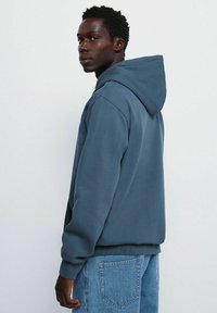 Haut à capuche bleu foncé avec cordon de serrage, poignets et ourlet côtelés, et coupe décontractée, associé à un jean bleu clair.