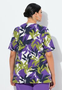 Camiseta con un patrón de hojas tropicales en púrpura y verde sobre un fondo blanco, de mangas cortas, corte holgado y escote redondo.