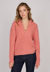 Pull en tricot rose avec une demi-fermeture éclair, texture côtelée et manches longues, associé à un jean en denim foncé.