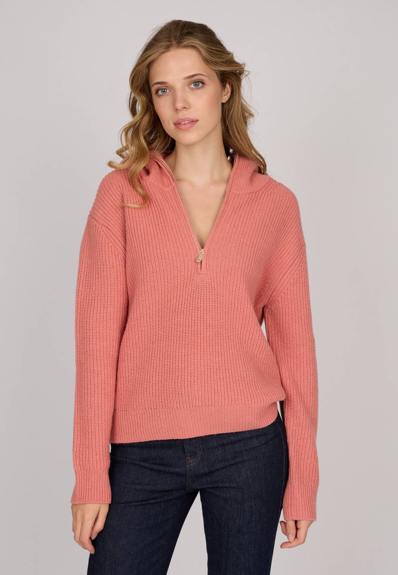 Pull en tricot rose avec une demi-fermeture éclair, texture côtelée et manches longues, associé à un jean en denim foncé.
