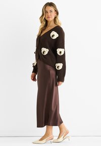 Brown knitted cardigan with bear motifs, paired with a brown satin midi skirt and cream slingback heels.