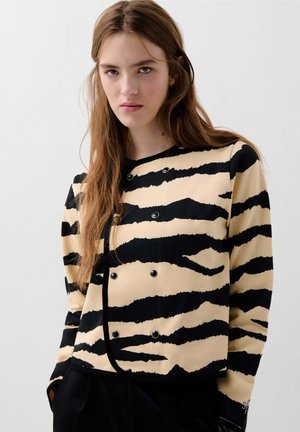 Afbaret jakke i beige med kraftige sorte tigermønstre, med dobbelbrystet design og sorte knapper, lavet af tekstureret stof.