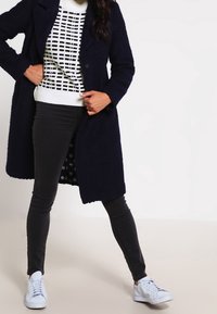 Marinblå herringbone-struktur coat, vit och svart rutmönstrad tröja, svarta skinny jeans och vita sneakers. Prickig foder synlig.