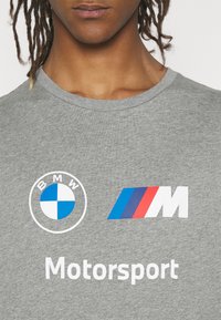Šedé bavlněné tričko s logem BMW, M pruhy v modré, červené a bílé barvě a slovem "Motorsport" v bílé barvě níže.