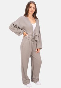 Hellgraues Zweiteiler-Outfit aus texturiertem Stoff. Besteht aus einer verkürzten Strickjacke mit Bindegürtel und weit geschnittenen Hosen mit Spitzenbesatz.