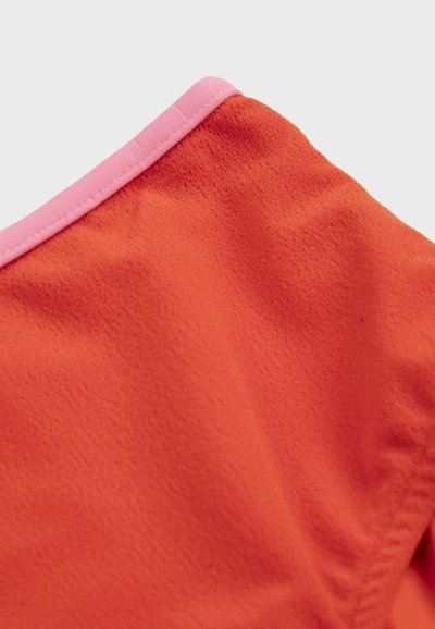 Tissu orange vif avec une texture douce et un bord rose cousu sur un fond clair uni.