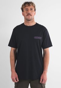T-shirt in cotone nero con logo viola sul lato sinistro del petto. Collo giroclassico e maniche corte con un fit rilassato.