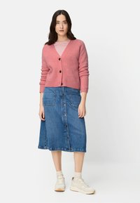 Różowy kardigan z mieszanki wełny z dekoltem w serek i zapinany na guziki, noszony na jasnej, paskowanej koszuli, zestawiony z dżinsową spódnicą w linii A i trampkami.