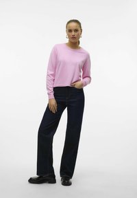 Top lungo in cotone rosa con scollatura rotonda, abbinato a pantaloni a gamba larga in denim blu scuro a vita alta e scarpe con plateau nere.