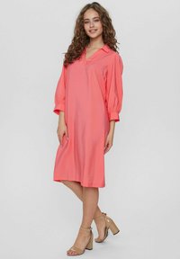 Rosa knälång klänning med V-ringning och korta puffärmar, tillverkad av mjukt tyg. Matchad med beige högklackade sandaler.