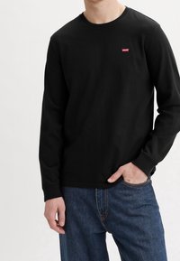 Camiseta de manga larga negra hecha de algodón, con escote redondo, puños acanalados y un pequeño logo rojo de Levi's en el pecho.