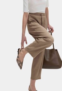 Light brown crepe trousers with a textured surface, wide legs, elastic waistband, and drawstring. Paired with reptile-patterned heels and a brown tote.