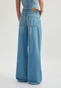 Jeans de pierna ancha de color azul claro, hechos de denim, con una cintura alta, dos bolsillos traseros y un parche de cuero marrón en la parte posterior.