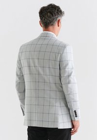 Jasnoszary marynarka w kratkę, wykonana z fakturowanej tkaniny, z zapięciem na dwa guziki i czarnymi guzikami, z jednym rozcięciem z tyłu.