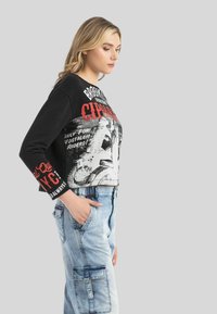 Schwarzer, cropped Sweatshirt mit grafischem Druck in Weiß und Rot, kombiniert mit hellblauen Denim-Cargohosen, die über mehrere Taschen und einen Reißverschluss verfügen.