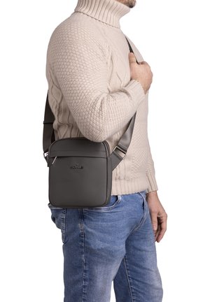 Borsa a spalla in pelle grigia con finitura liscia, forma quadrata, tasca frontale con zip e tracolla regolabile, indossata a tracolla.