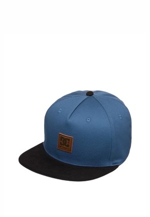 Niebieska czapka typu snapback z czarnym płaskim daszkiem i małą brązową skórzaną naszywką w kształcie kwadratu z logo na przedniej części.