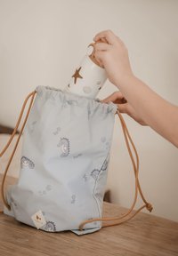 Vaaleansininen narureppu merihevoskuvioilla, ruskeilla nyörikoristeilla, sisältäen valkoisen vesipullon, joka on koristeltu meritähdillä ja simpukoilla.