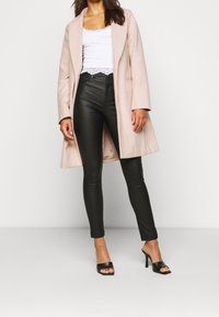 Light pink long coat, white lace-trimmed tank top, black high-waisted leather pants, and black open-toe heels. Smooth textures, fitted design.
