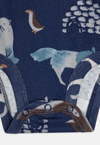 Mornarsko modra bodysuit z motivi divjih živali, vključno s ptico in vidro. Ima gumbe za zapiranje in mehko, teksturirano bombažno tkanino.