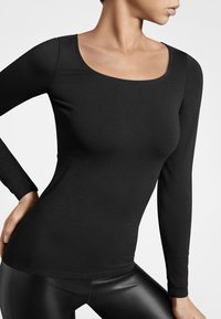 Svart långärmad topp med rundad halsringning, tillverkad av slät, figurnära material, i kombination med stilrena svarta leggings.